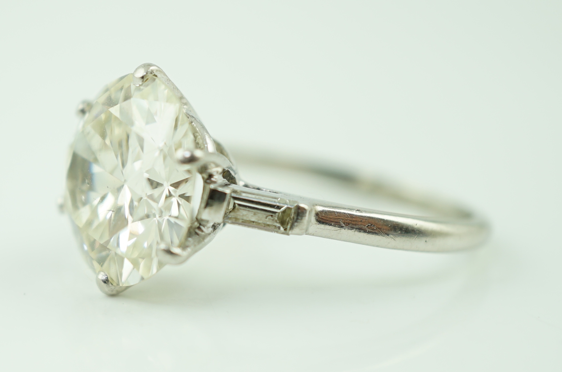 A platinum and single stone diamond set ring, with baguette cut diamond set shoulders